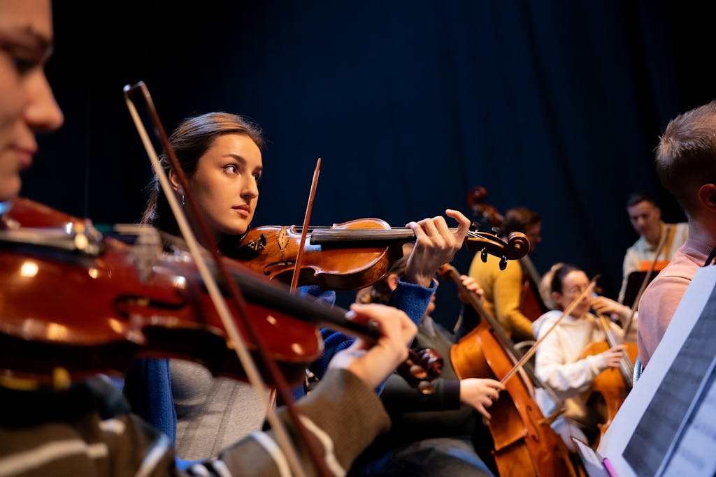 A group of musicians perform in an orchestra, featuring a violinist in focus.