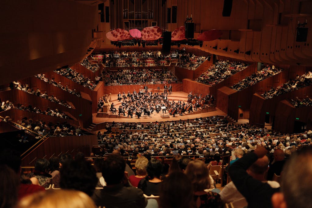 A large audience enjoys a symphony orchestra performance at the iconic Sydney Opera House.